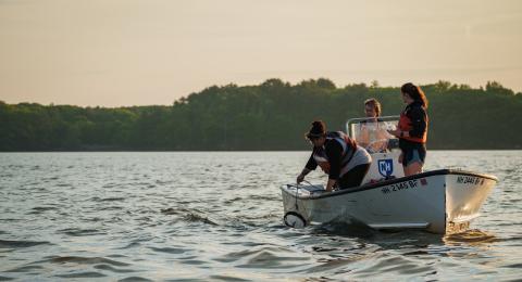 Three researchers are in a small boat at sunrise