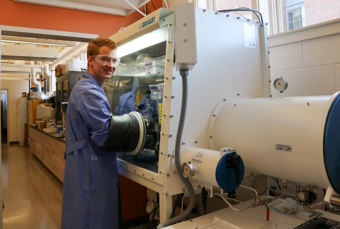 Graduate student Nick Pollack wears a lab coat and puts his arms inside a machine