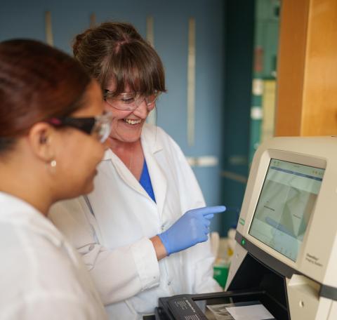 two women in white lab coats looking at an instrument screen