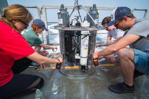 Four researchers crouch at stern of research vessel with scientific equipment