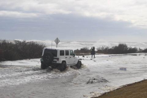 Coastal flooding White jeep driving through flood water along coast