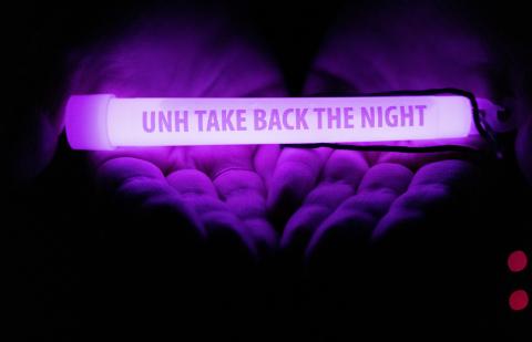 two open palm hands holding a purple glowstick that reads UNH take back the night