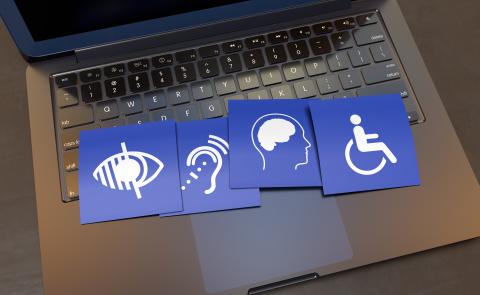 Picture of an open laptop computer with cards on the keyboard that depict various accessibility symbols, including a wheelchair, a brain, an ear, and an eye.