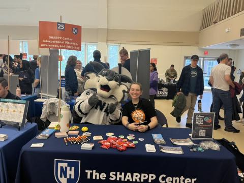 A student sits at a SHARPP Center table next to UNH's mascot, Wild E. Cat