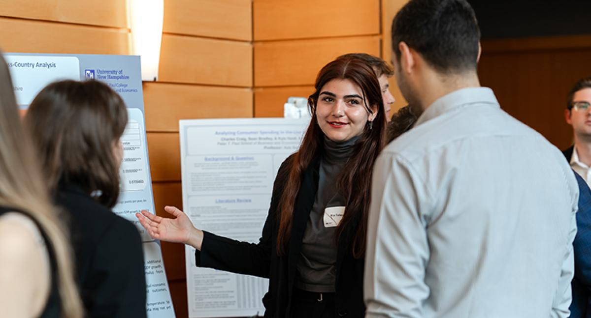 A woman points to a poster while speaking to a man and a woman