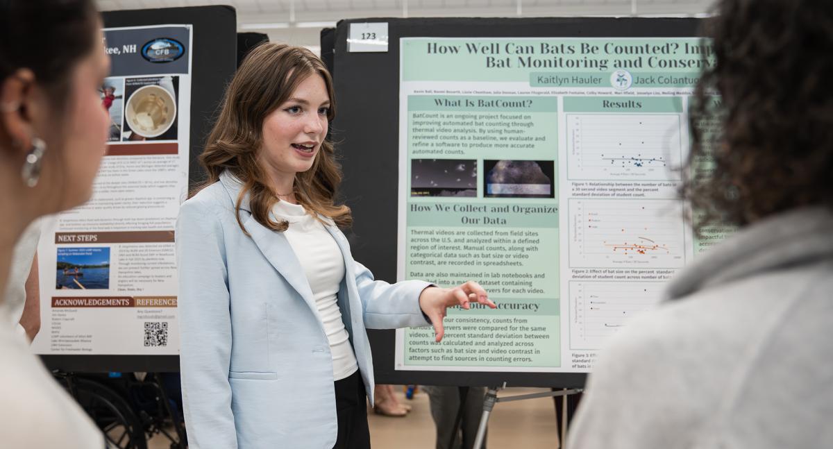A woman in a light blue blazer speaks to two onlooking woman while making a presentation