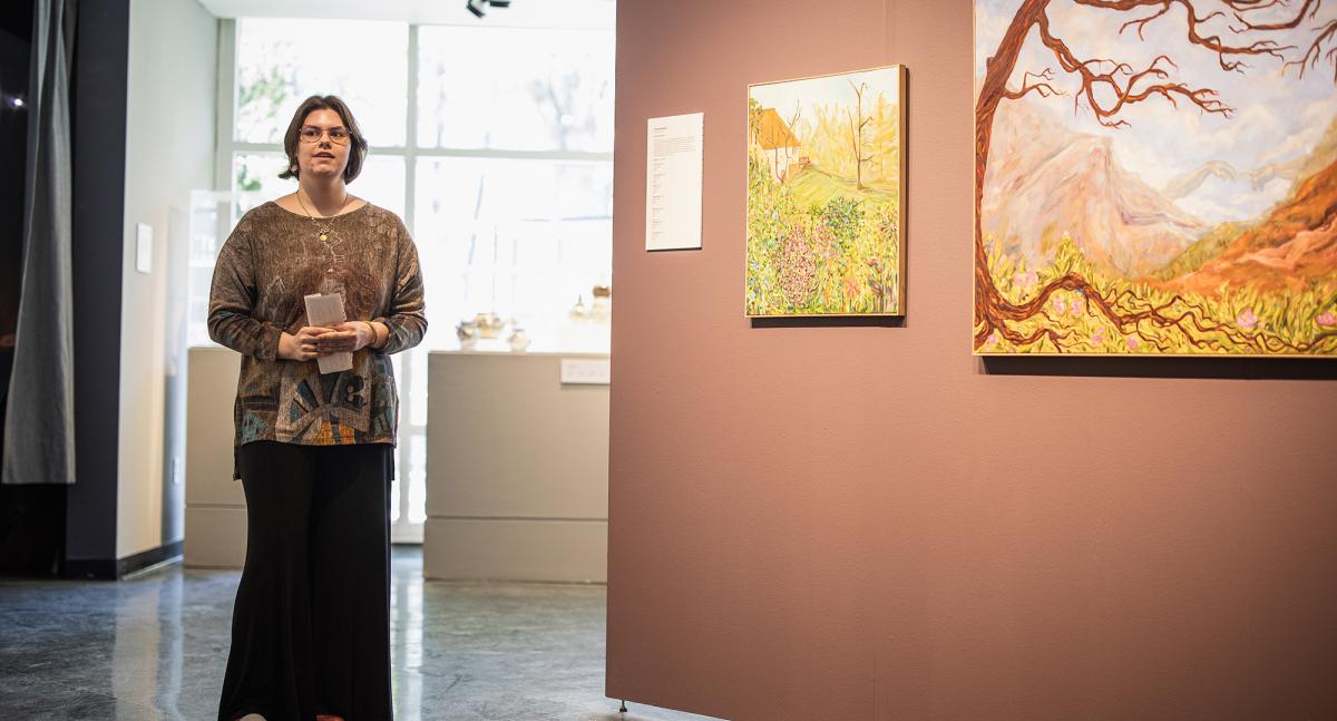 A woman stands alongside colorful artwork on the wall of a gallery