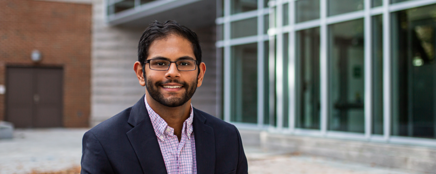 A male student smiles at the camera while seated in Paul College's outdoor courtyard.