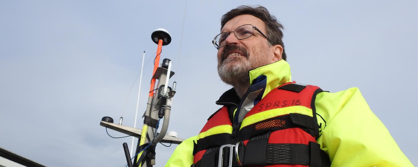 Brian Calder wears a life jacket and holds a remote controller while aboard a boat. 
