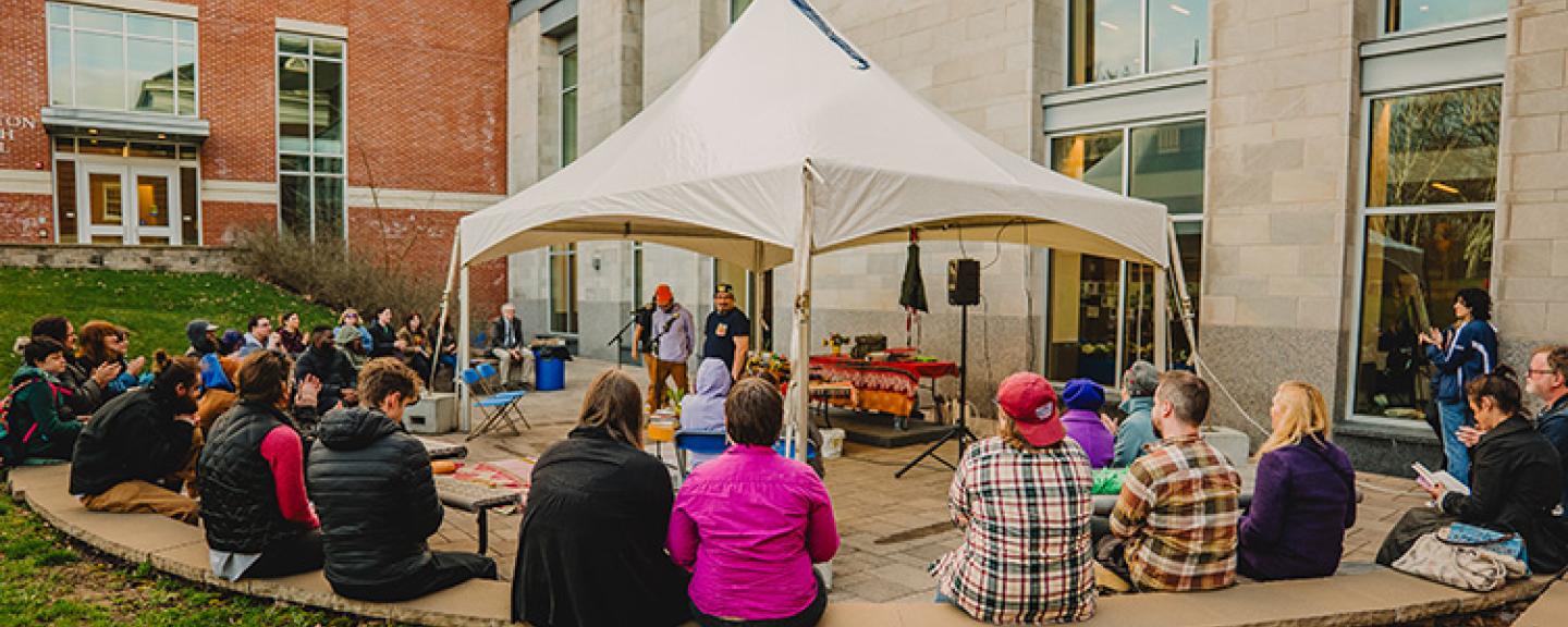 A crowd sits in a semi circle around a small stage with two performers