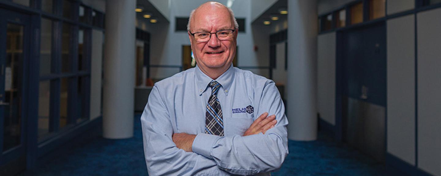 Man wearing a light blue shirt and a tie smiles for a portrait