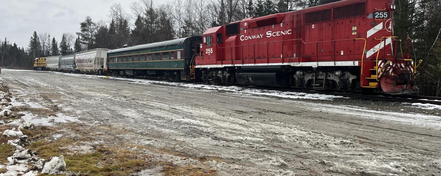 A locomotive pulling several passenger cars is shown on tracks.