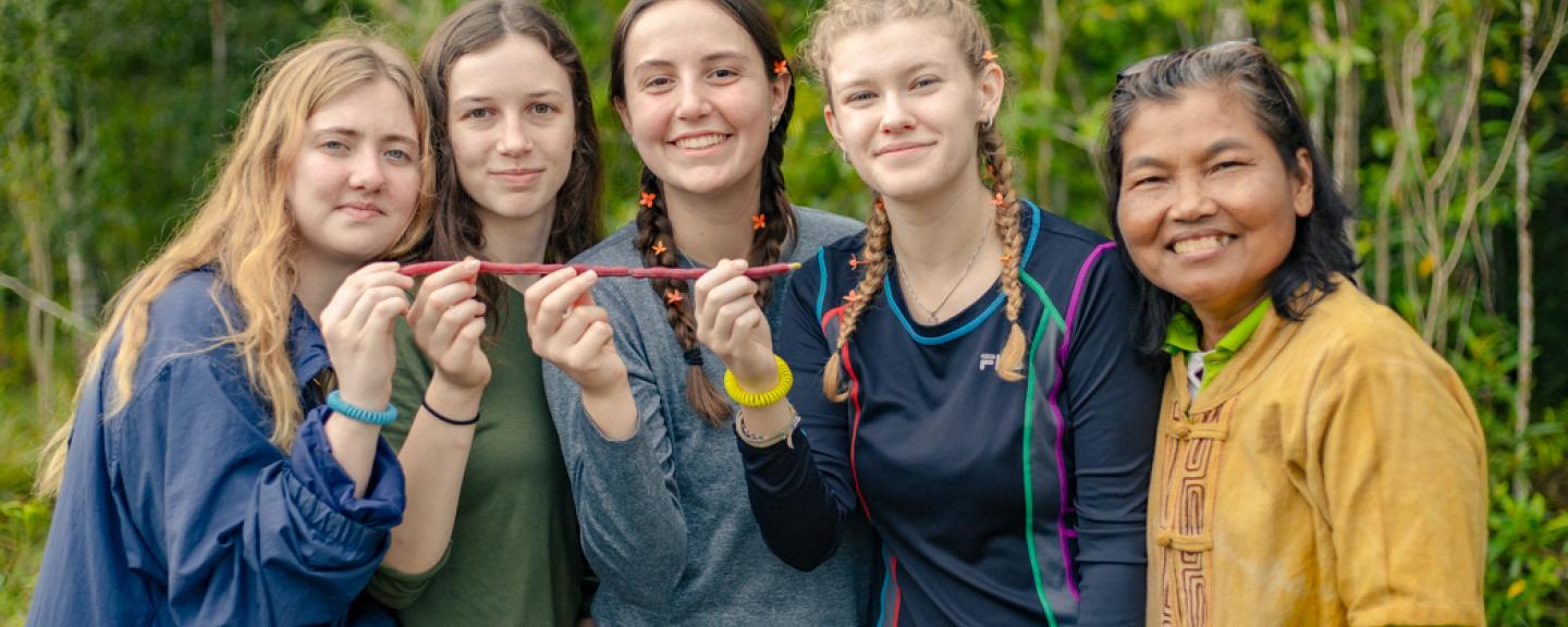 five people standing side by side outside smiling and some are holding a red stick