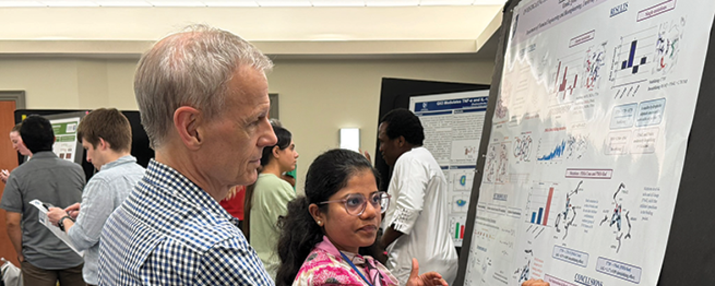Rick Cote stands next to a student while she describes the work featured in her research poster