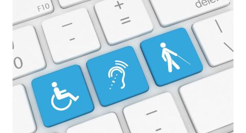 Close up view of a computer keyboard. Three keys are light blue. One has a symbol of a person in a wheelchair. One has a symbol for assistive listening. One has a symbol of a person walking with a cane.