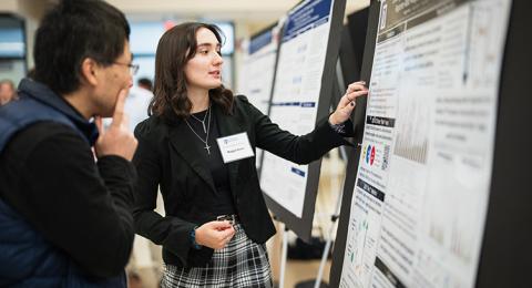 Female student points to a poster while explaining its content to a male to her left