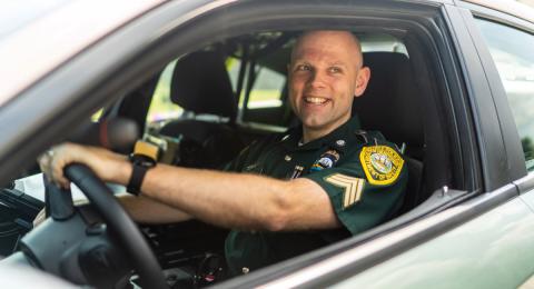 A male police officer sitting in the driver's seat of a police car