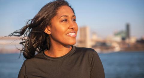 close up of a woman looking off into the distance with the skyline of new york city behind her