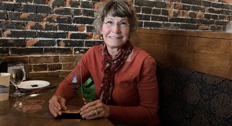Karla Armenti sits in a restaurant booth holding an award and smiling