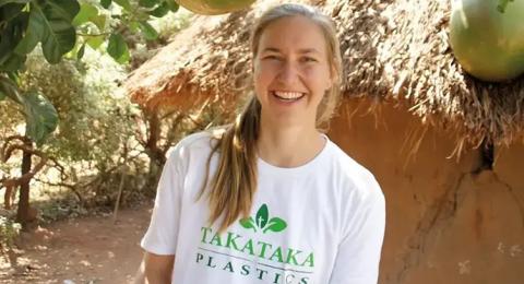 A woman in a white T-shirt stands in front of trees in Africa