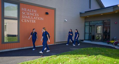 Students in blue scrubs walk alongside the Health Sciences Simulation Center