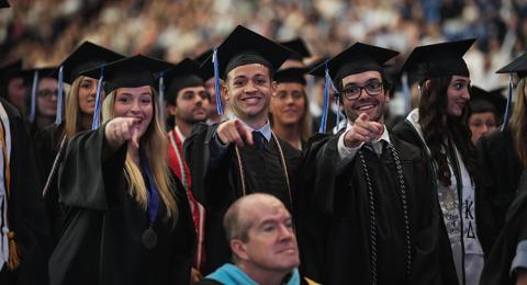 Three graduates point toward the camera at commencement