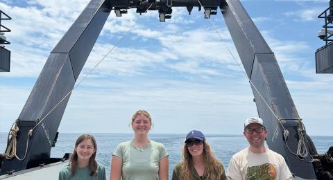 Three female students and one male researcher stand on board a research vessel.