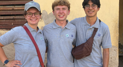 three people standing side by side outside in front of a building