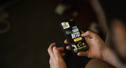 A person holds a smartphone displaying an online sports betting app.