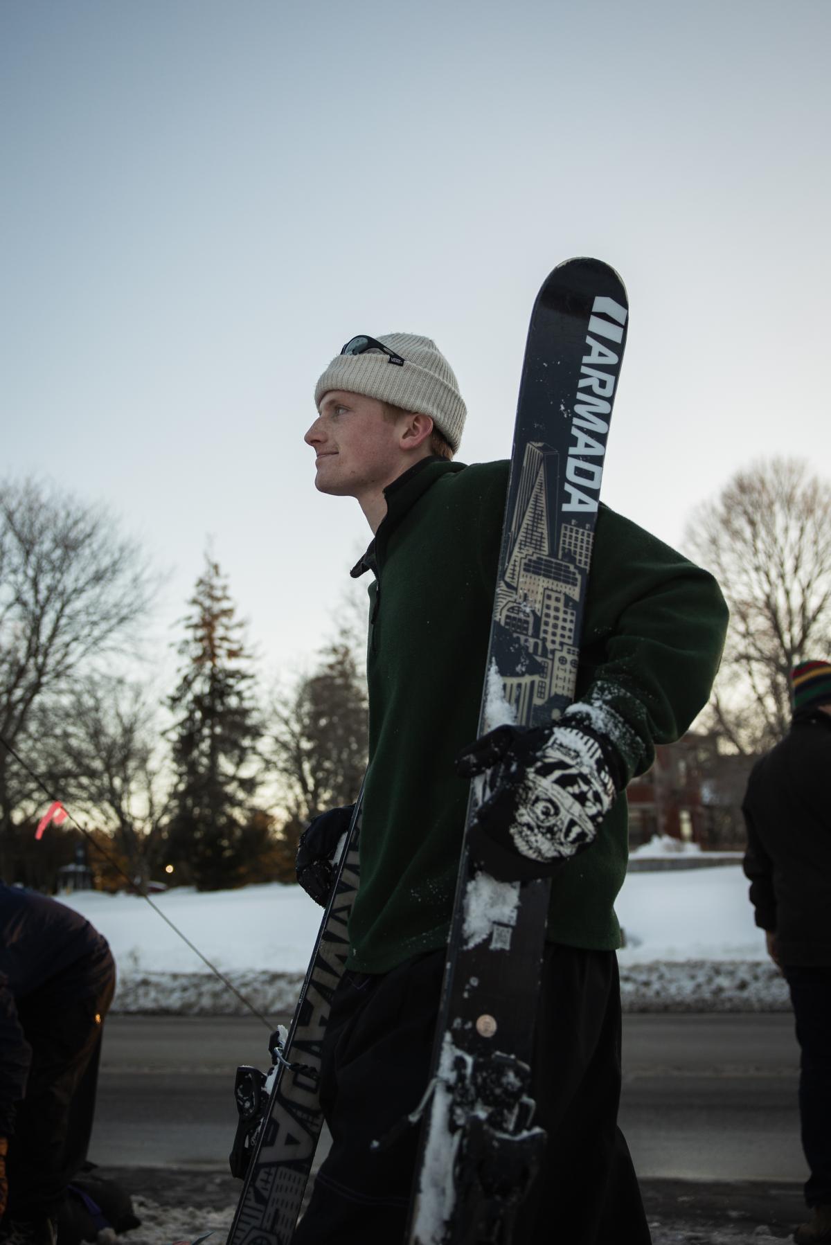A man in a winter hat walks with his skis by his side