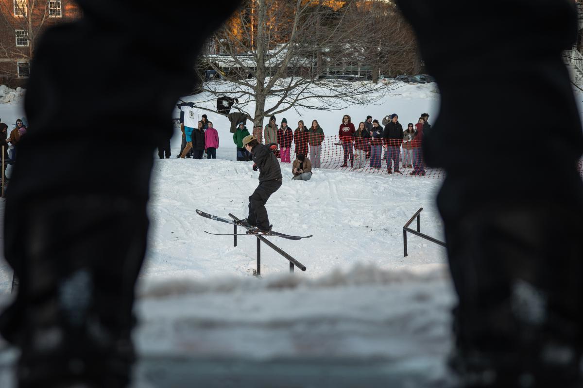 A skier is visible between two arches in the foreground as he rides along a rail