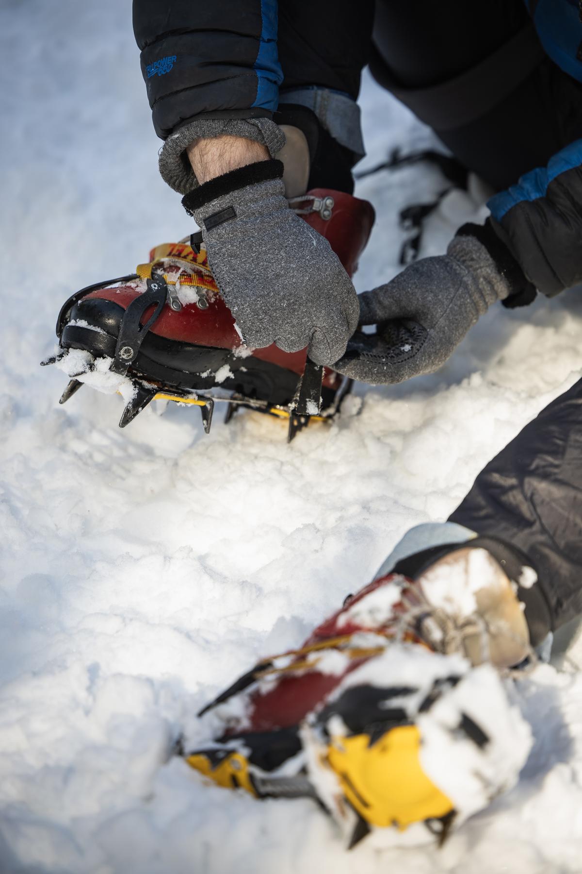 A close up image of a hand in gray gloves removing crampons from a boot