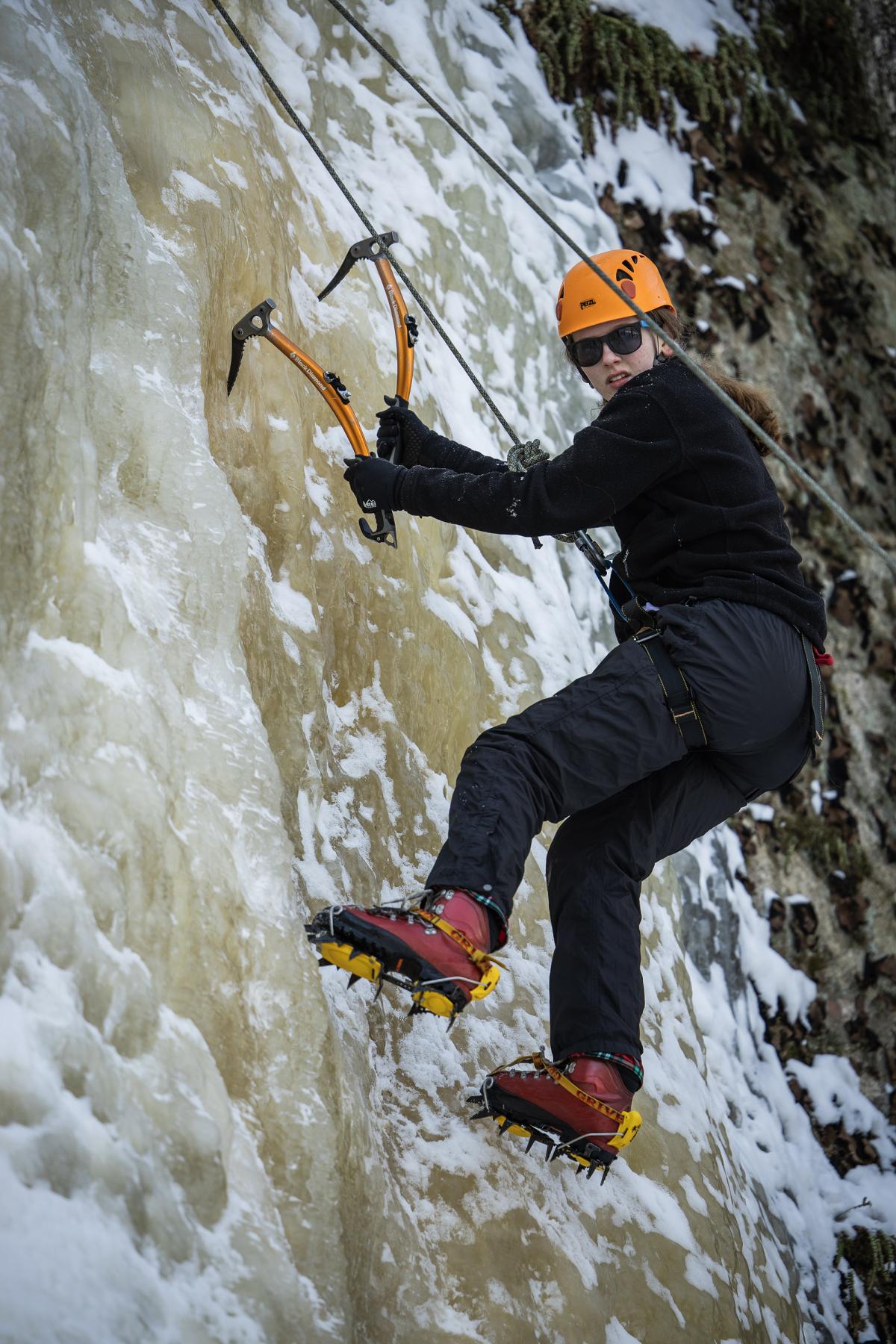 A student looks toward the camera while ice climbing