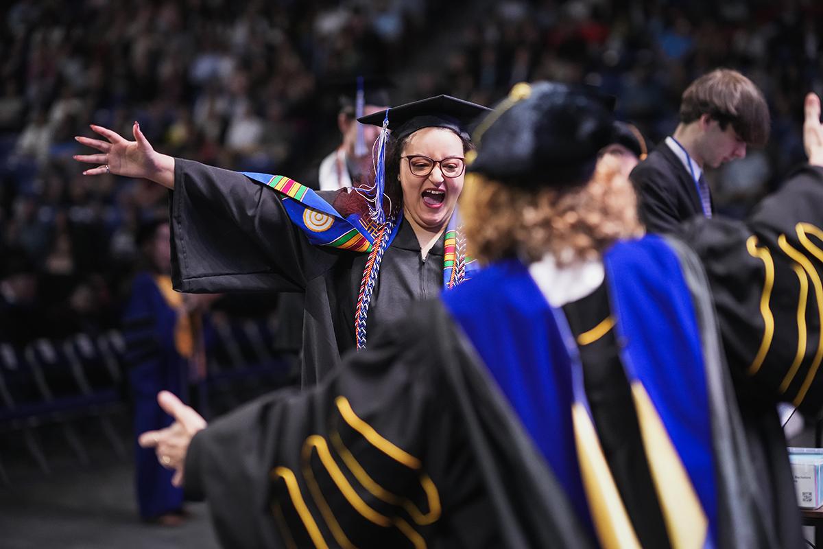 A woman graduate approaches the stage with her arms outstretched for a hug
