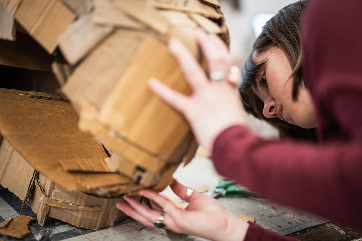 A student works on a cardboard mask during sculpture class