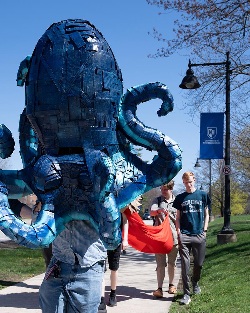 A student wears a large mask created in their sculpture class during a campus parade