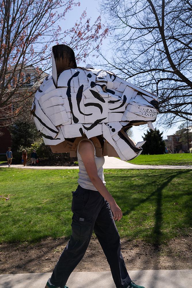 A student wears a large mask created in their sculpture class during a campus parade
