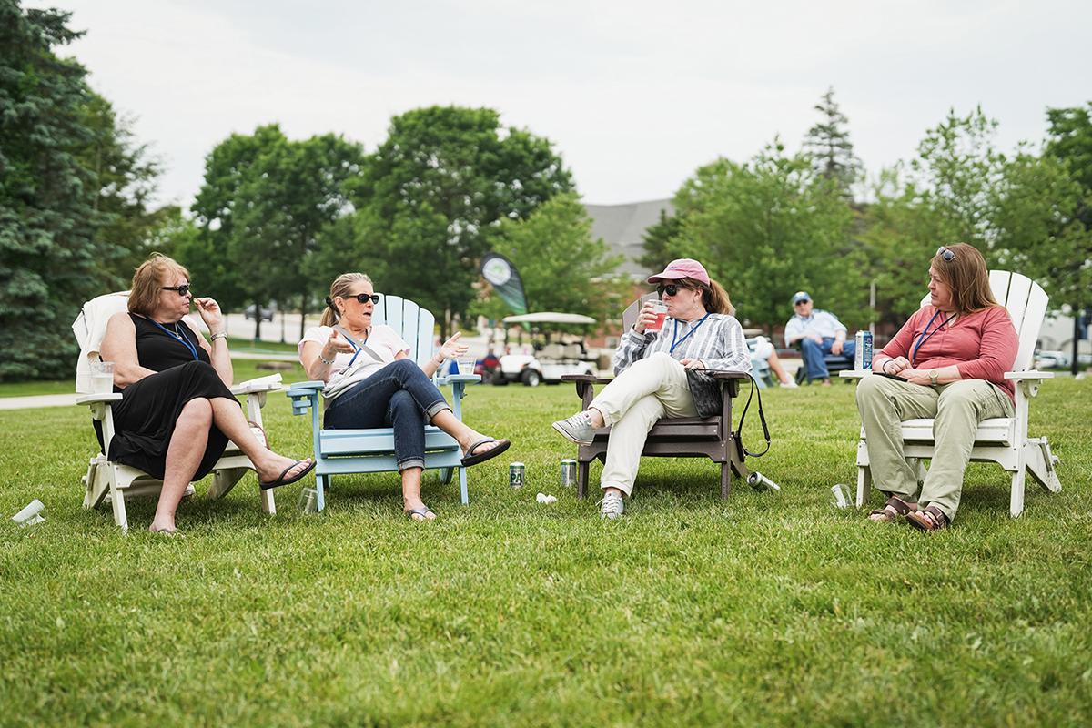 Four women sit in Adirondack chairs at reunion
