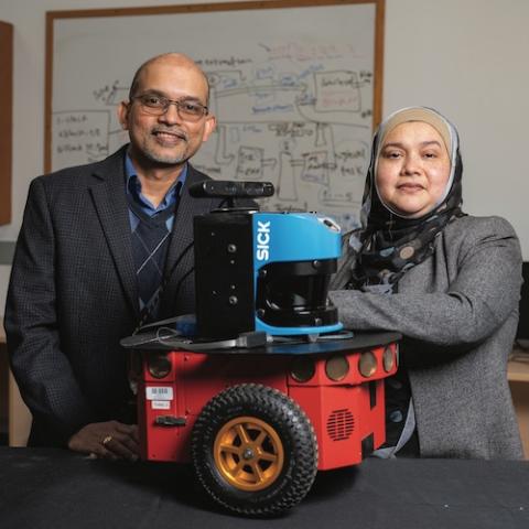 A male and female researcher stand with arms crossed in front of a small robot