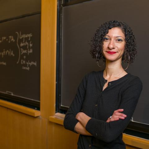 Female professor stands with arms crossed in front of chalkboard