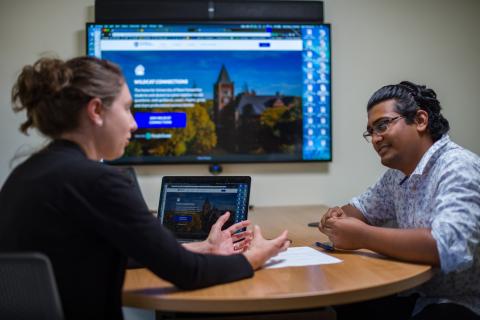 Two people discussing business with a laptop and screen at a small wooden table