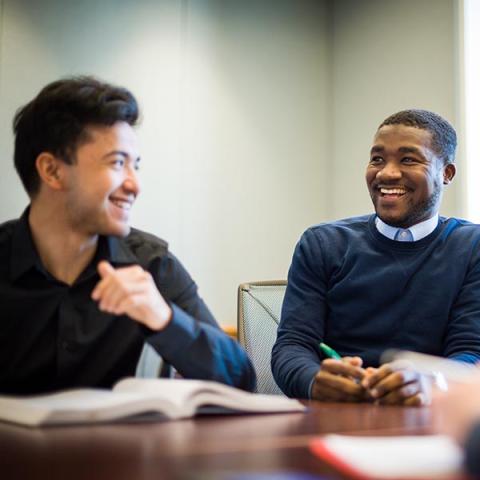 UNH Graduate students talking at table with textbook