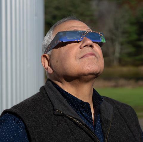Male space scientist wearing eclipse glasses looks toward the sky