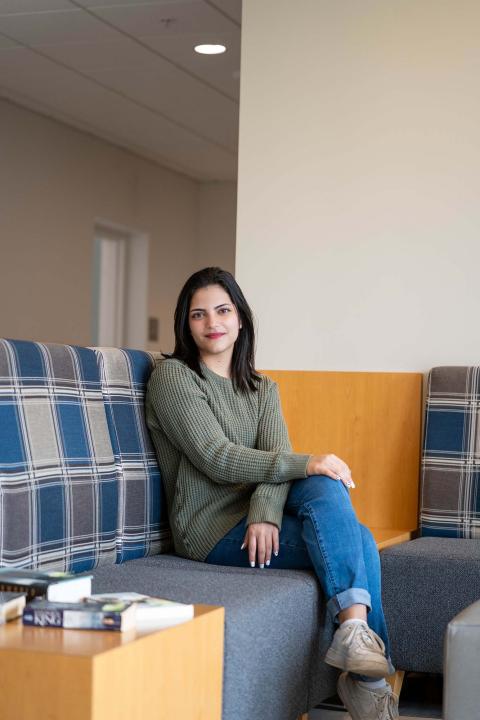 Analytical economics major Dija Haq sits on a couch in the UNH MUB, legs crossed, with a small smile for the camera.