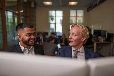 Two male students laugh at each other in UNH Paul College's bloomberg terminal room.
