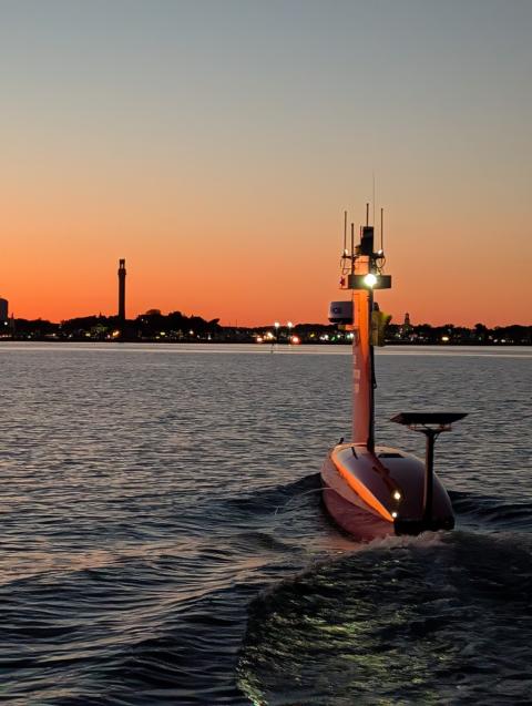 Autonomous vessel in the water at sunset with cityscape behind