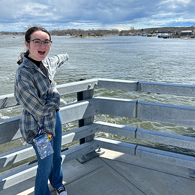 UNH student Jess Calarese standing on a deck outside pointing to the ocean in the background