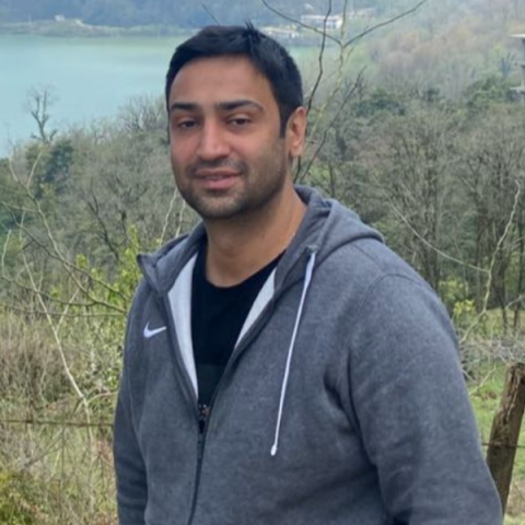 person standing outside with a field and body of water in the background