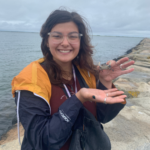 person standing outside by a large body of water holding a crab in one hand