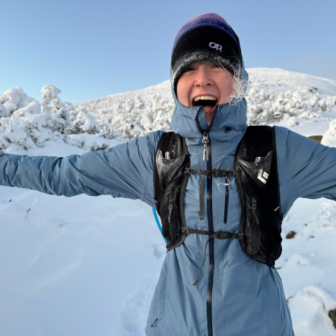 person standing outside smiling with snowy mountains in the background